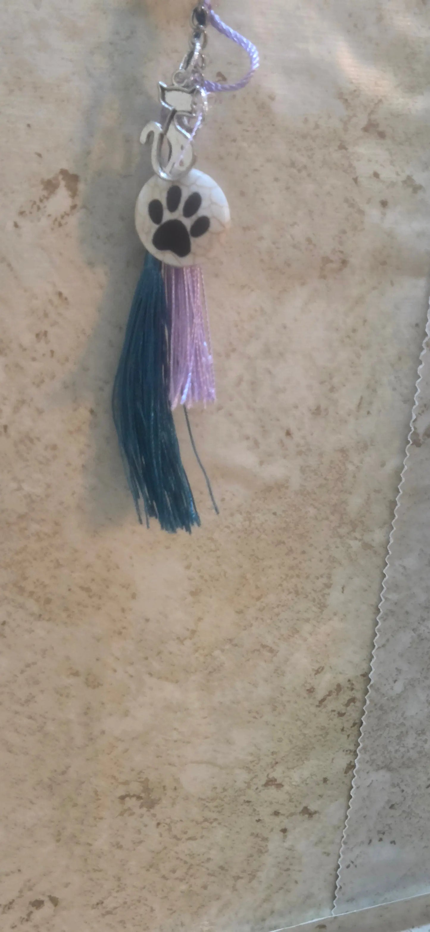 Round white stone with black pow print and a silver cat charm and a teal and lavender tassels keuyhains - Crazy Cat Lady Crafts