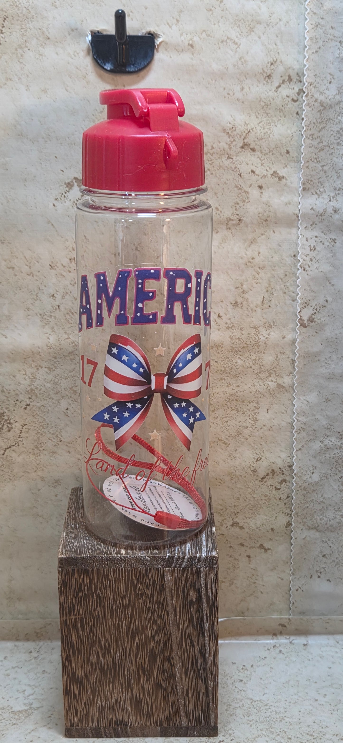 17 ounce clear water bottle with red flip top lid and strap with a red white and blue ribbon and saying