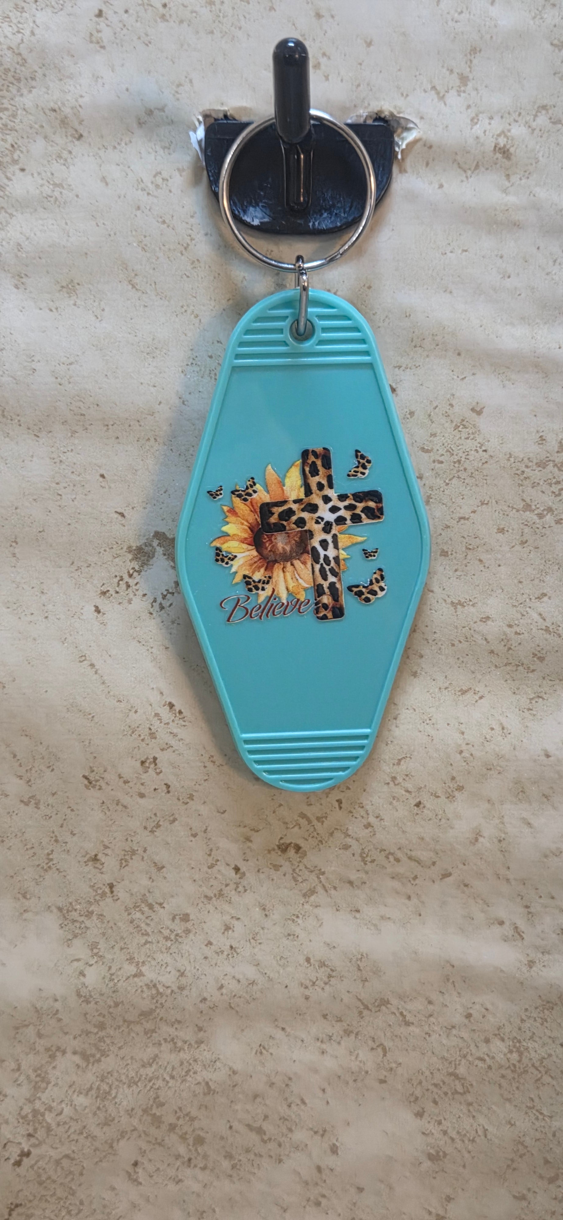 Plastic replica of a motel key with leopard skin cross and sunflower says believe